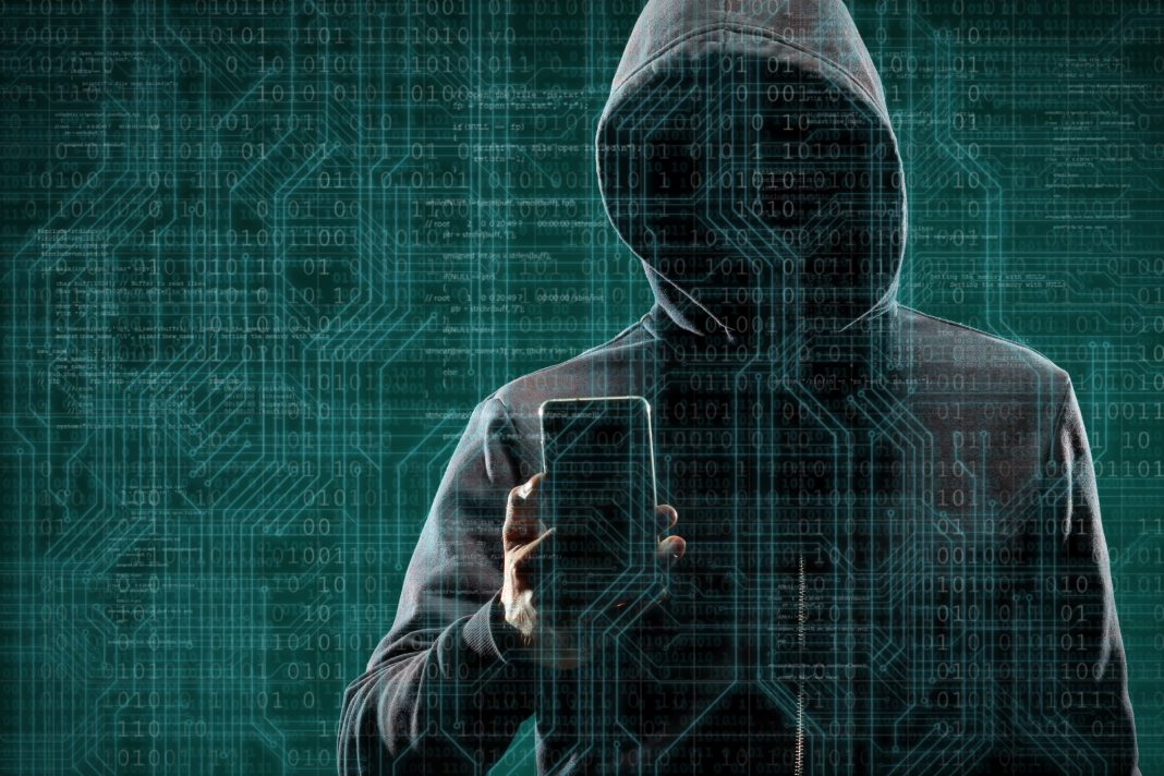 Anonymous computer hacker with a smartphone over abstract digital background. Obscured dark face in mask and hood. Data thief, internet attack, darknet fraud, dangerous viruses and cyber security.